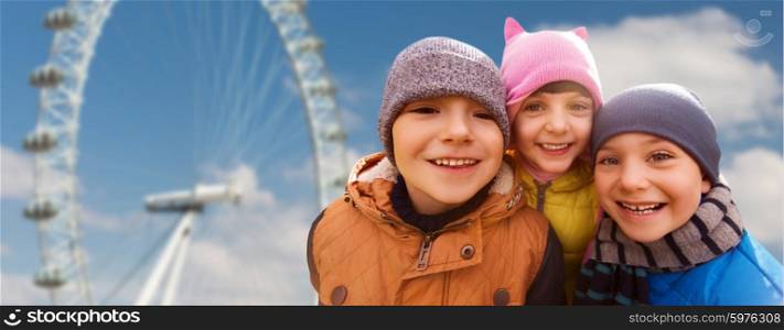 childhood, tourism, travel, vacation and people concept - happy little children outdoors over ferry wheel and blue sky background