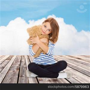 childhood, toys and people concept - cute little girl hugging teddy bear over blue sky and cloud background