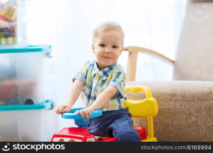 childhood, toys and people concept - happy little baby boy driving ride-on toy car at home
