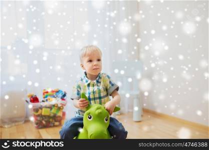 childhood, toys and people concept - happy little baby boy playing with ride-on toy horse at home over snow