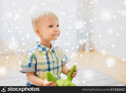 childhood, toys and people concept - happy little baby boy playing with ride-on toy horse at home over snow