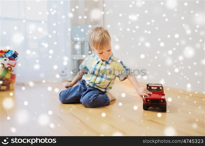childhood, toys and people concept - little baby boy playing with toy car at home over snow