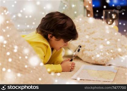 childhood, travel and christmas concept - happy little boy with magnifier and road map searching location in kids tent at home over snow. boy with magnifier and map in kids tent at home