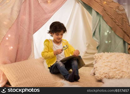 childhood, travel and hygge concept - happy little boy with magnifier and road map searching location in kids tent at home. boy with magnifier and map in kids tent at home. boy with magnifier and map in kids tent at home