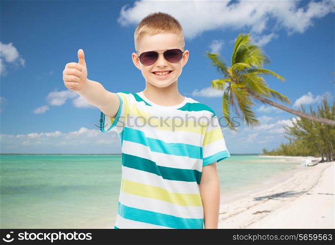 childhood, travel, summer vacation, gesture and people concept - smiling little boy wearing sunglasses over beach background
