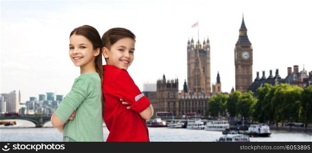 childhood, travel, tourism and people concept - happy smiling boy and girl standing back to back over london city background