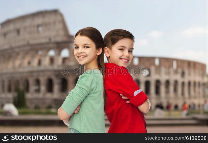 childhood, travel, tourism and people concept - happy smiling boy and girl standing back to back over coliseum in rome
