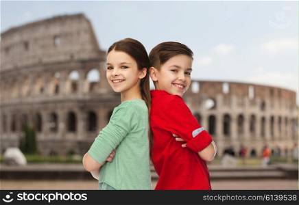 childhood, travel, tourism and people concept - happy smiling boy and girl standing back to back over coliseum in rome