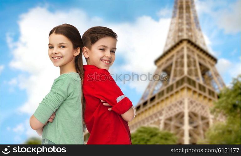 childhood, travel, tourism, and people concept - happy smiling boy and girl standing back to back over paris eiffel tower background