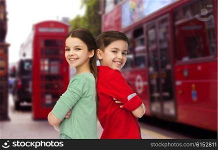 childhood, travel, tourism, and people concept - happy smiling boy and girl standing back to back over london city street background
