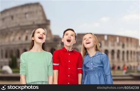 childhood, travel, tourism, emotions and people concept - happy amazed boy and girls looking up with open mouths over coliseum in rome
