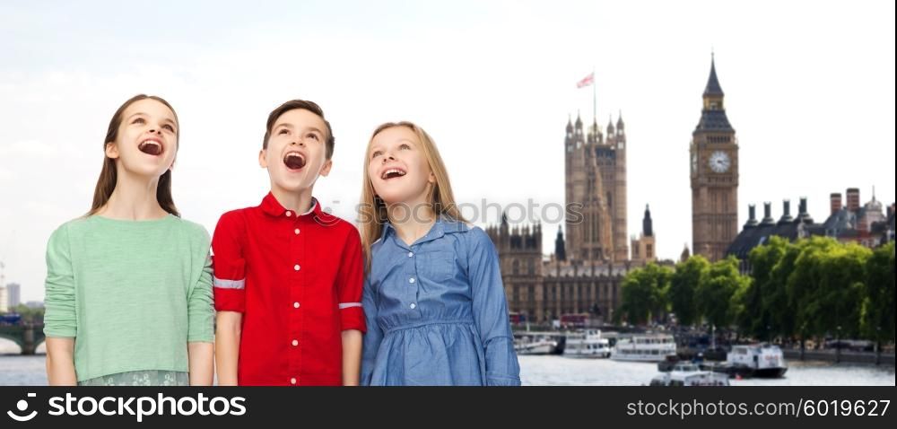childhood, travel, tourism, friendship and people concept - happy amazed boy and girls looking up with open mouths over london city background