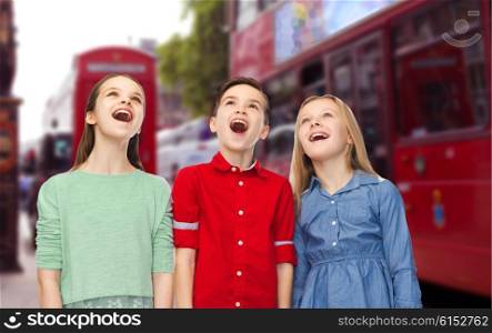 childhood, travel, tourism, friendship and people concept - happy amazed boy and girls looking up with open mouths over london city street background