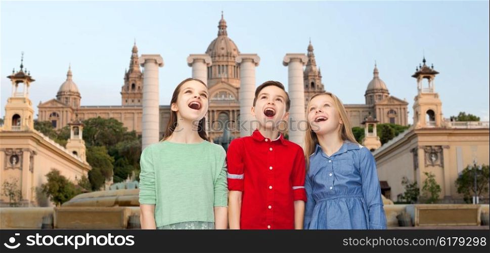 childhood, travel, tourism, friendship and people concept - happy amazed boy and girls looking up with open mouths over national museum of barcelona background