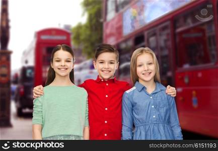 childhood, travel, tourism, friendship and people concept - happy smiling boy and girls hugging over london city street background