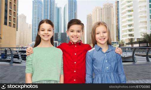childhood, travel, tourism, friendship and people concept - happy smiling children hugging over dubai city street background