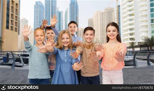childhood, travel, tourism, gesture and people concept - group of happy children waving hands over dubai city street background