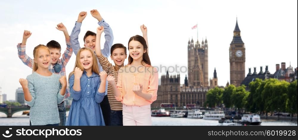 childhood, travel, tourism, gesture and people concept - happy children friends raising fists and celebrating victory over london city background