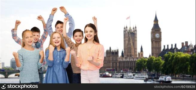 childhood, travel, tourism, gesture and people concept - happy children friends raising fists and celebrating victory over london city background