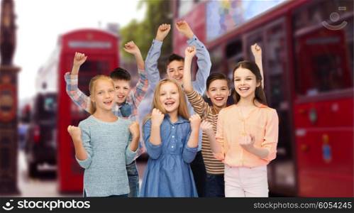childhood, travel, tourism, gesture and people concept - happy children friends raising fists and celebrating victory over london city street background