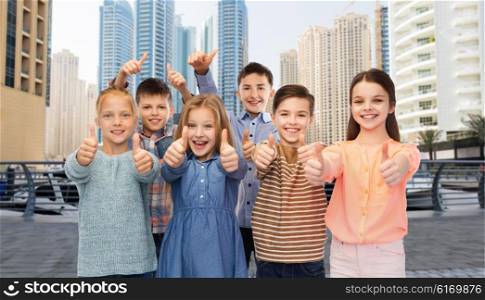 childhood, travel, tourism, gesture and people concept - happy smiling boy and girls showing thumbs up over dubai city street background