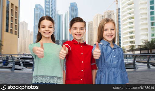 childhood, travel, tourism, gesture and people concept - happy smiling boy and girls showing thumbs up over dubai city street background