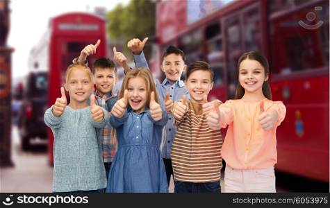 childhood, travel, tourism, gesture and people concept - happy smiling children showing thumbs up over london city street background