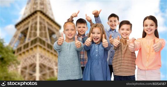 childhood, travel, tourism, gesture and people concept - happy smiling children showing thumbs up over paris eiffel tower background