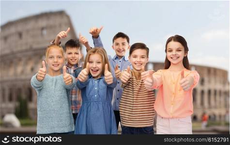childhood, travel, tourism, gesture and people concept - happy smiling children showing thumbs up over coliseum in rome
