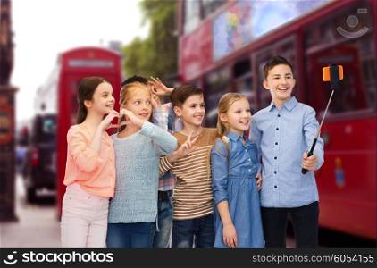 childhood, travel, tourism, technology and people concept - happy children talking picture by smartphone on selfie stick over london city street background