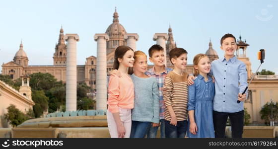 childhood, travel, tourism, technology and people concept - happy children talking picture by smartphone on selfie stick ovetrnational museum of barcelona background