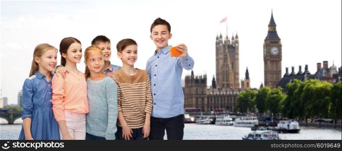 childhood, travel, tourism, technology and people concept - happy children talking selfie by smartphone over london city background