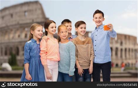 childhood, travel, tourism, technology and people concept - happy children talking selfie by smartphone over coliseum in rome