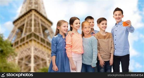 childhood, travel, tourism, technology and people concept - happy children talking selfie by smartphone over paris eiffel tower background