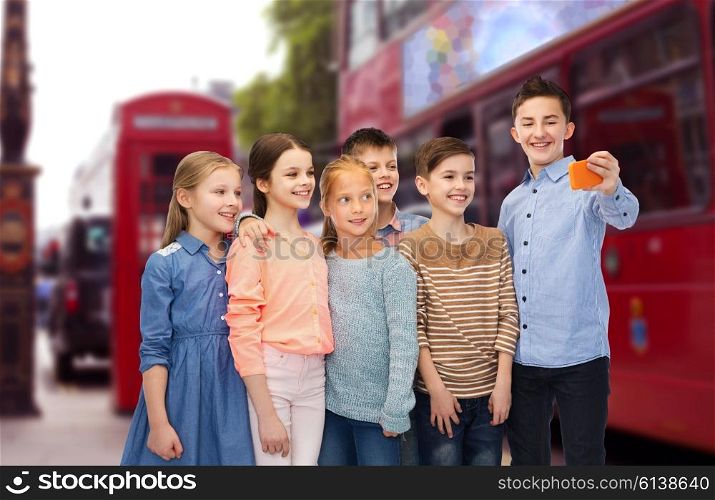 childhood, travel, tourism, technology and people concept - happy children talking selfie by smartphone over london city street background