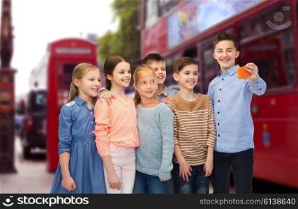 childhood, travel, tourism, technology and people concept - happy children talking selfie by smartphone over london city street background