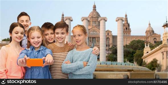 childhood, travel, tourism, technology and people concept - happy children talking selfie by smartphone over national museum of barcelona background