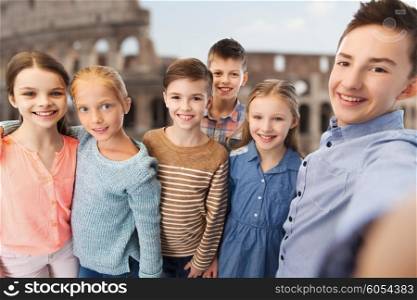 childhood, travel, tourism, technology and people concept - happy children talking selfie over coliseum in rome