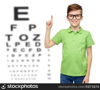 childhood, vision, eyesight and people concept - happy smiling boy in green polo t-shirt in eyeglasses pointing finger up over eye chart background