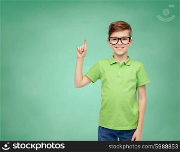 childhood, vision, school, education and people concept - happy smiling boy in green polo t-shirt in eyeglasses pointing finger up over green school chalk board background