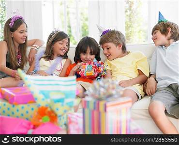 Children (7-12) sitting on sofa watching one open birthday present