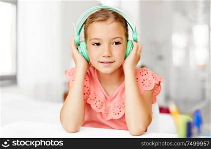 children and technology concept - happy girl in headphones listening to music at home desk. girl in headphones listening to music at home