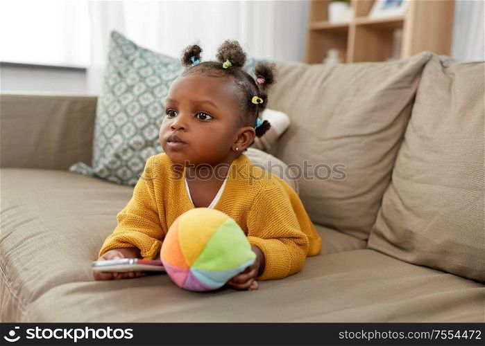 children and technology concept - lovely african american baby girl with smartphone and toy ball at home. african american baby girl with smartphone at home