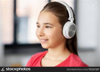 children and technology concept - portrait of smiling teenage girl in headphones listening to music at home. girl in headphones listening to music at home