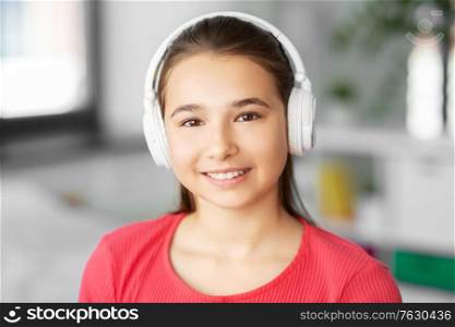 children and technology concept - portrait of smiling teenage girl in headphones listening to music at home. girl in headphones listening to music at home
