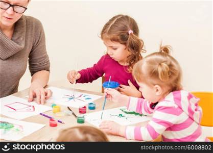 Children and tutor are painting with a brush and watercolors on paper in the kindergarten. Children are painting