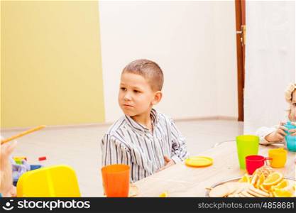 Children are sitting at the table with lunch and eating fruits and cakes. Lunch in kindergarden