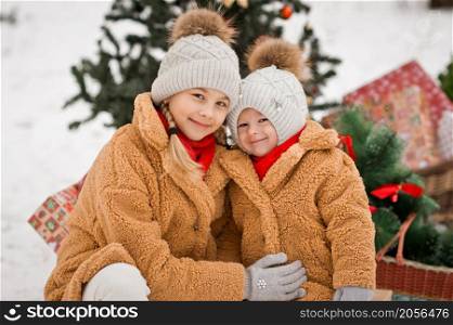 Children are sitting on gifts near the Christmas tree with balloons in the forest in winter.. Children play with gifts next to a decorated Christmas tree in a winter sno