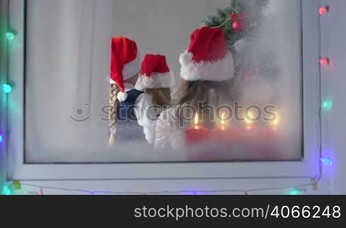 Children at home decorating Christmas tree view through the window