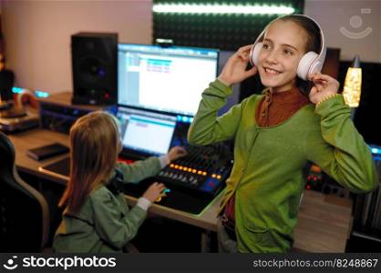 Children at recording studio, focus on young girl sound producer listening music in wireless headphones. Children at record studio focus on girl listening music in headset